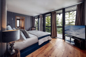 Bed in middle of room facing two floor to ceiling windows looking out over slopes